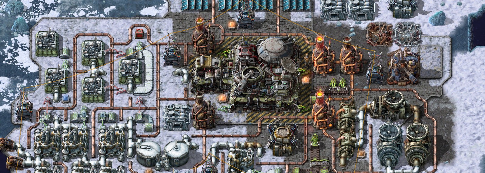 A Factorio base on the frozen planet Aquilo: machines, heat pipes and insulated pipe runs laid out on grey platform flooring surrounded by snow and cracked ice, with orange heating towers, a large central machine on yellow-striped concrete, and turbines at the right